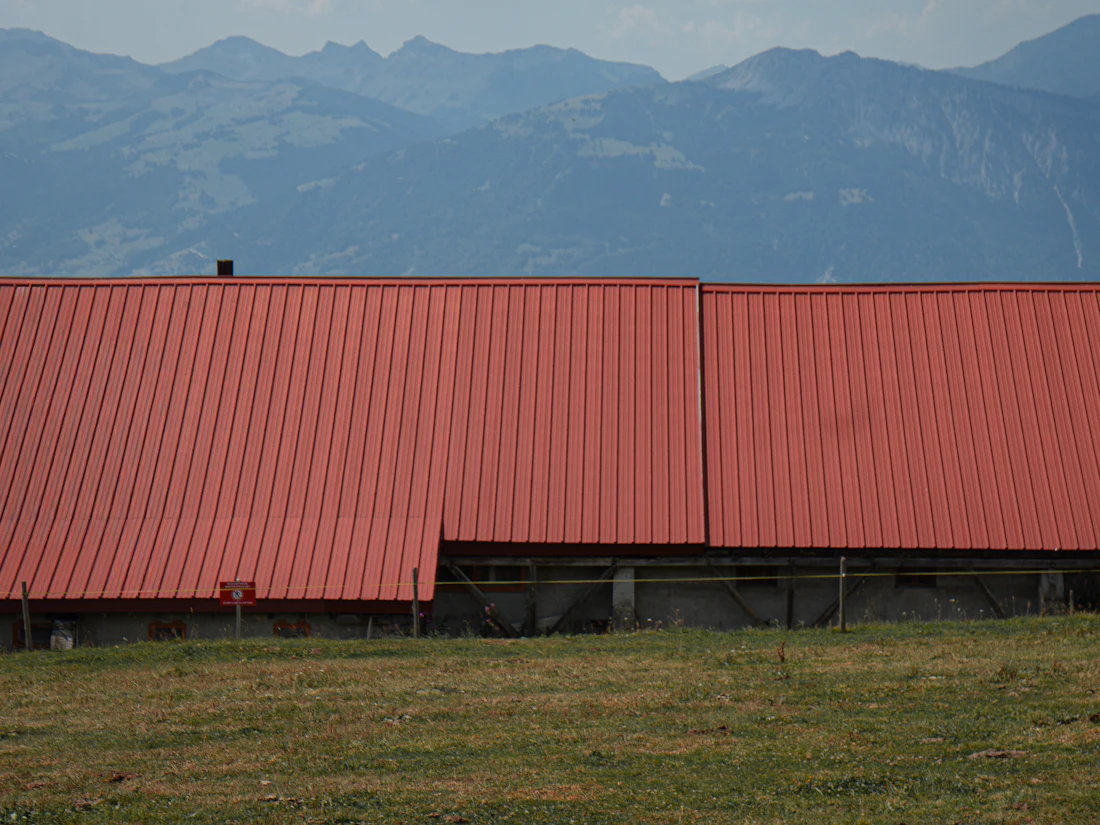 Long red metal roof on a farm building with mountains in the distance