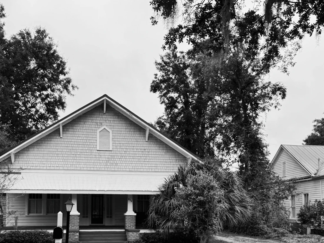 Older craftsman-style house with a steep gable roof and a front porch, in black and white