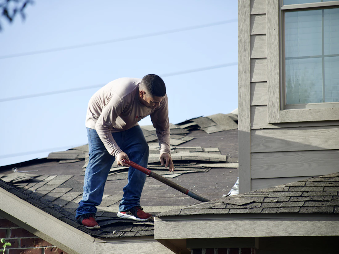 Roofer tearing off old asphalt shingles from a house roof