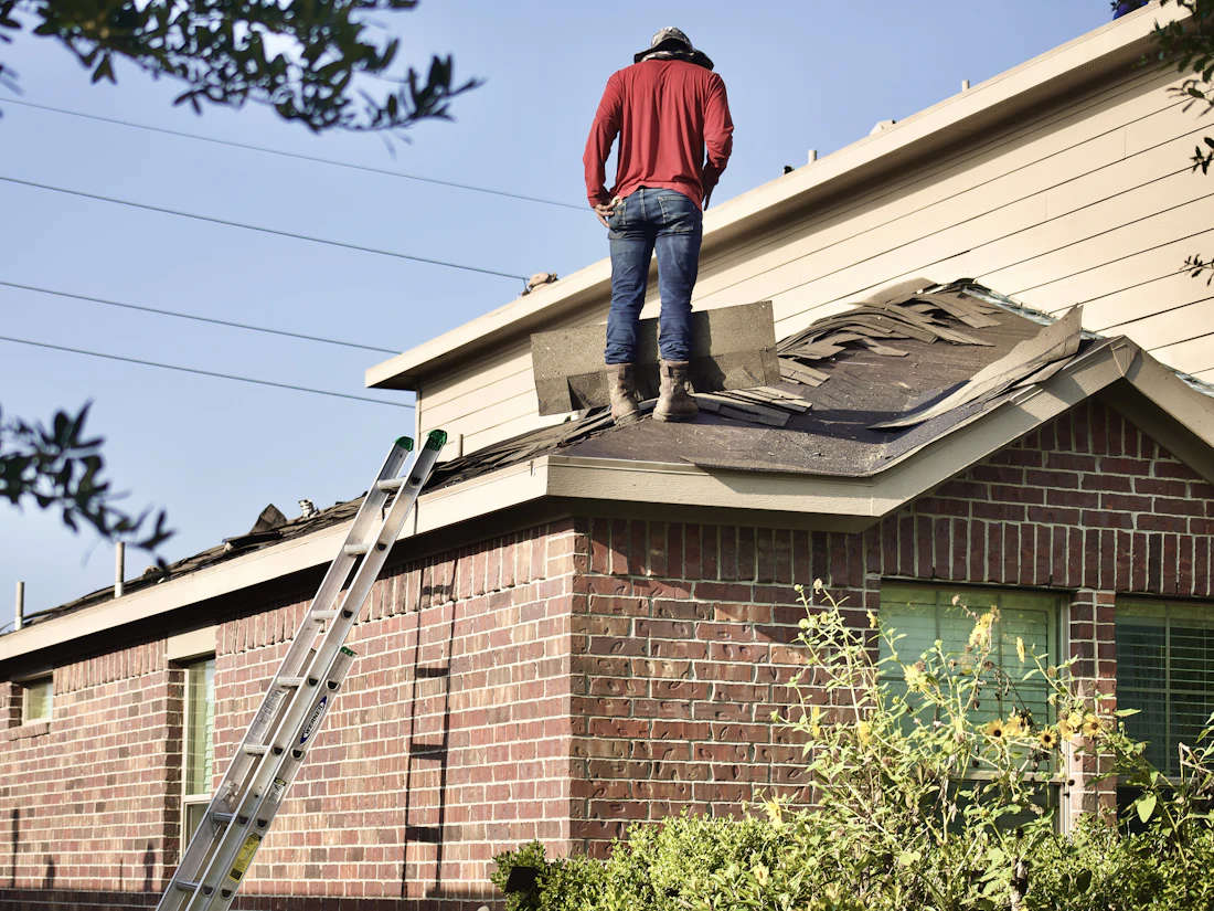 Roofer standing on a residential roof beside a ladder