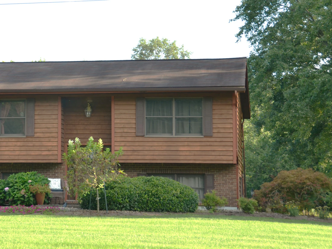 Brown split-level house with a shingle roof behind a green lawn
